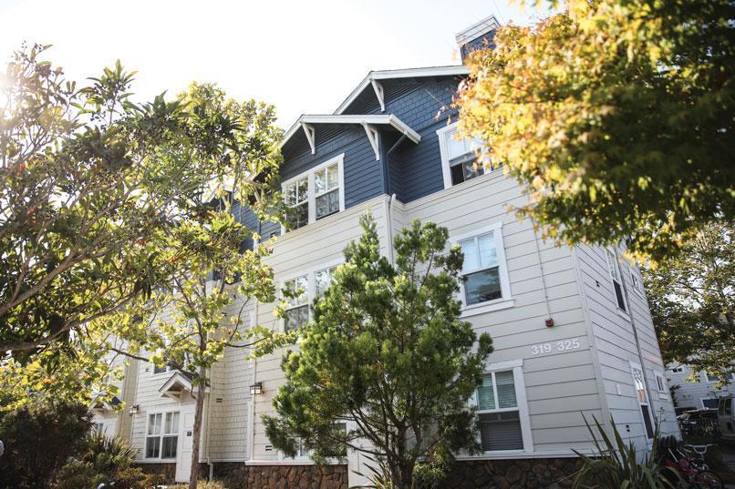 A multi-story, blue-and-white building stands amidst lush trees and sunlight. Visible numbers on the building read "319-325."