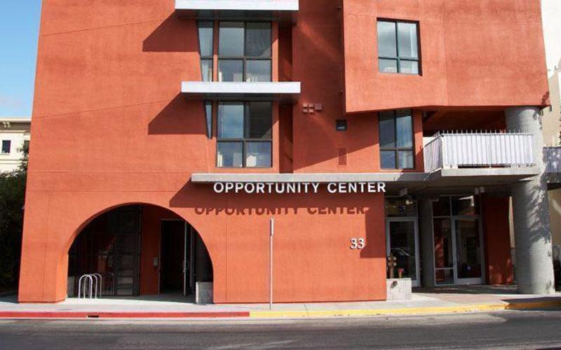 A building with orange-red facade displays the text "OPPORTUNITY CENTER 33." Two arched doorways are visible, and the structure includes multiple windows in an urban setting.