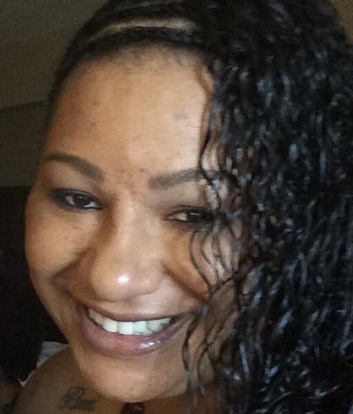 </p>
<h3>Brandi Andino</h3>
<p> A person smiling with braided and curly hair, displaying a tattoo on the shoulder, in an indoor setting with dim lighting.